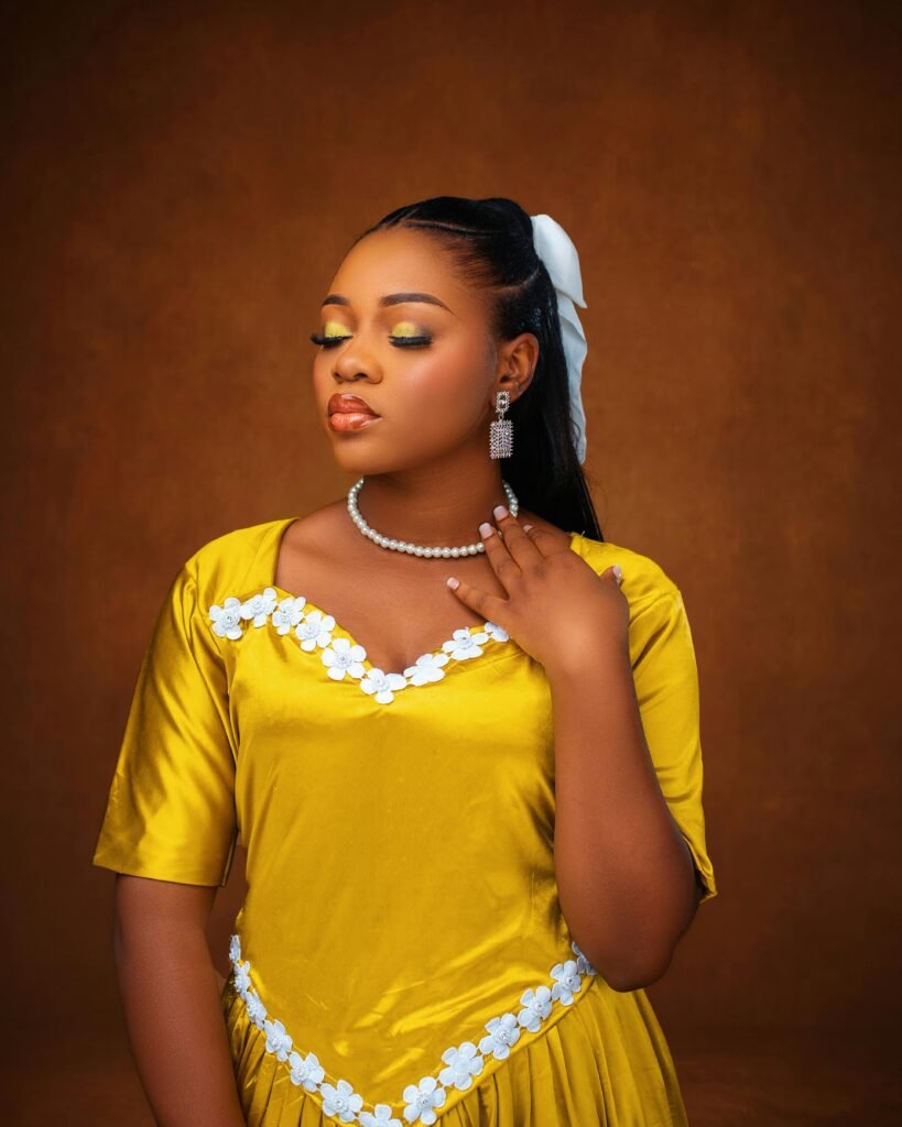 Stylish portrait of a woman in a bright yellow dress with elegant jewelry, set against a warm backdrop.